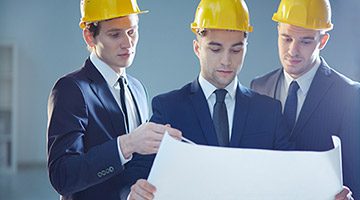 Three men in suits wearing yellow hardhats