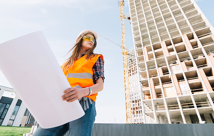 A woman wearing a white hardhat holding construction plans